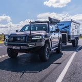SUV towing a camper trailer on a road with a clear sky.