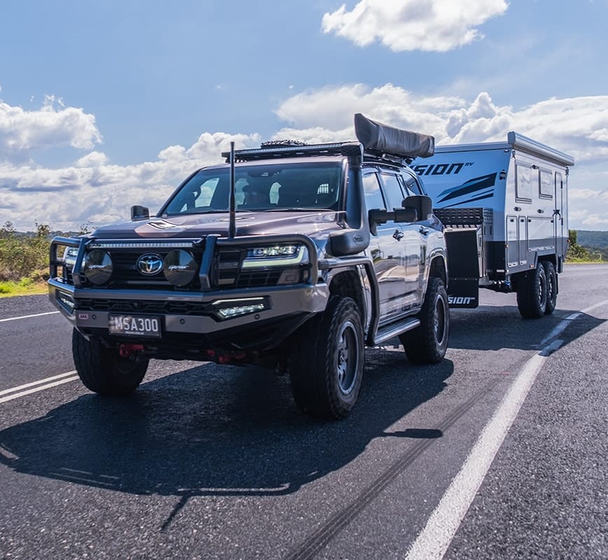 SUV towing a camper trailer on a road with a clear sky.