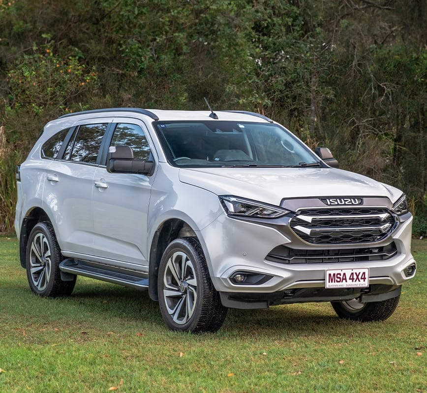 Silver Isuzu SUV parked on grass with trees in the background