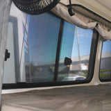 Close-up of an RV window with a fan and curtains