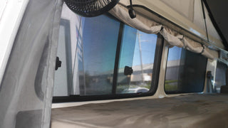 Close-up of an RV window with a fan and curtains