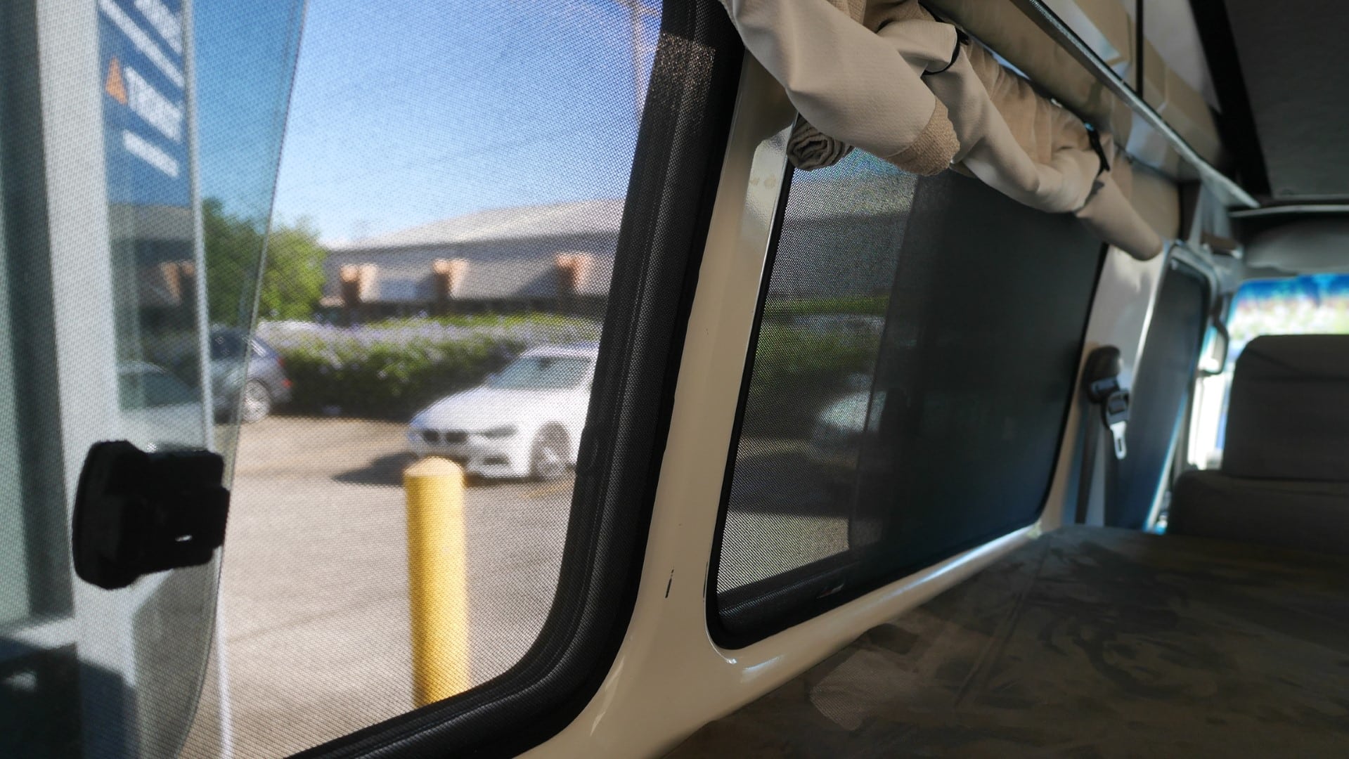 Interior view of a vehicle with open window and curtains, showing a parking lot outside.