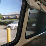 Interior view of a vehicle with open window and curtains, showing a parking lot outside.