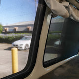 Interior view of a vehicle with open window and curtains, showing a parking lot outside.