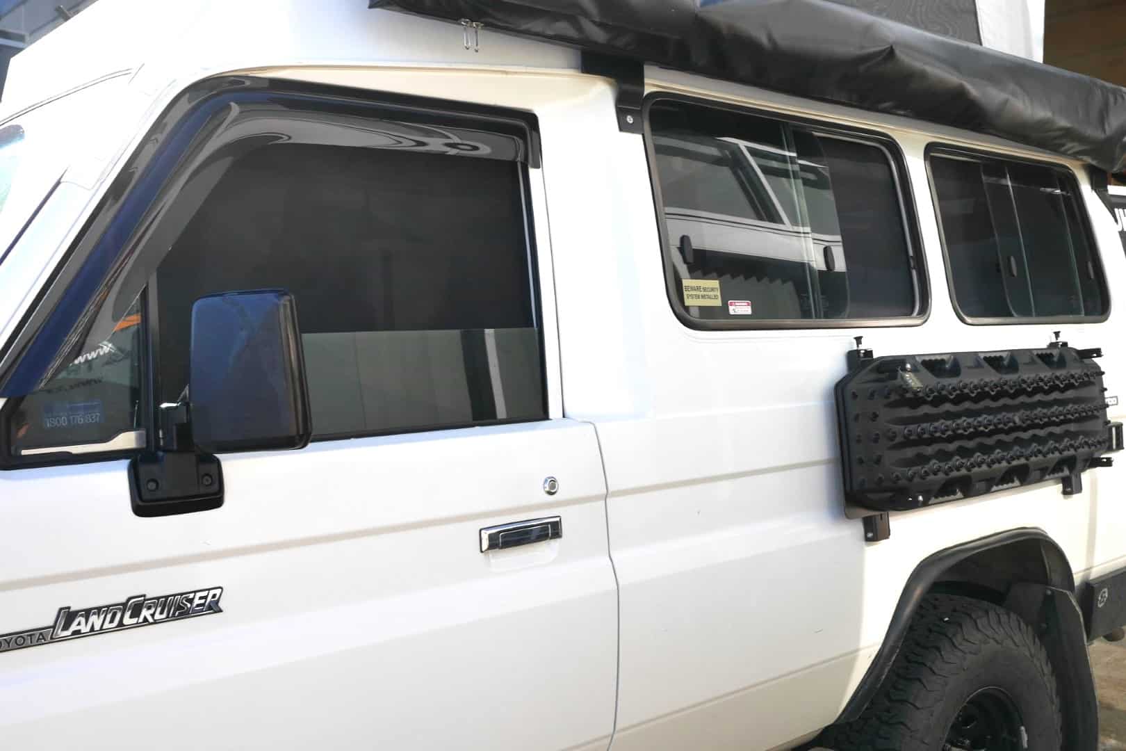 White Land Cruiser vehicle with black roof rack and side windows