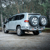 Silver SUV with spare tires on a gravel road surrounded by trees