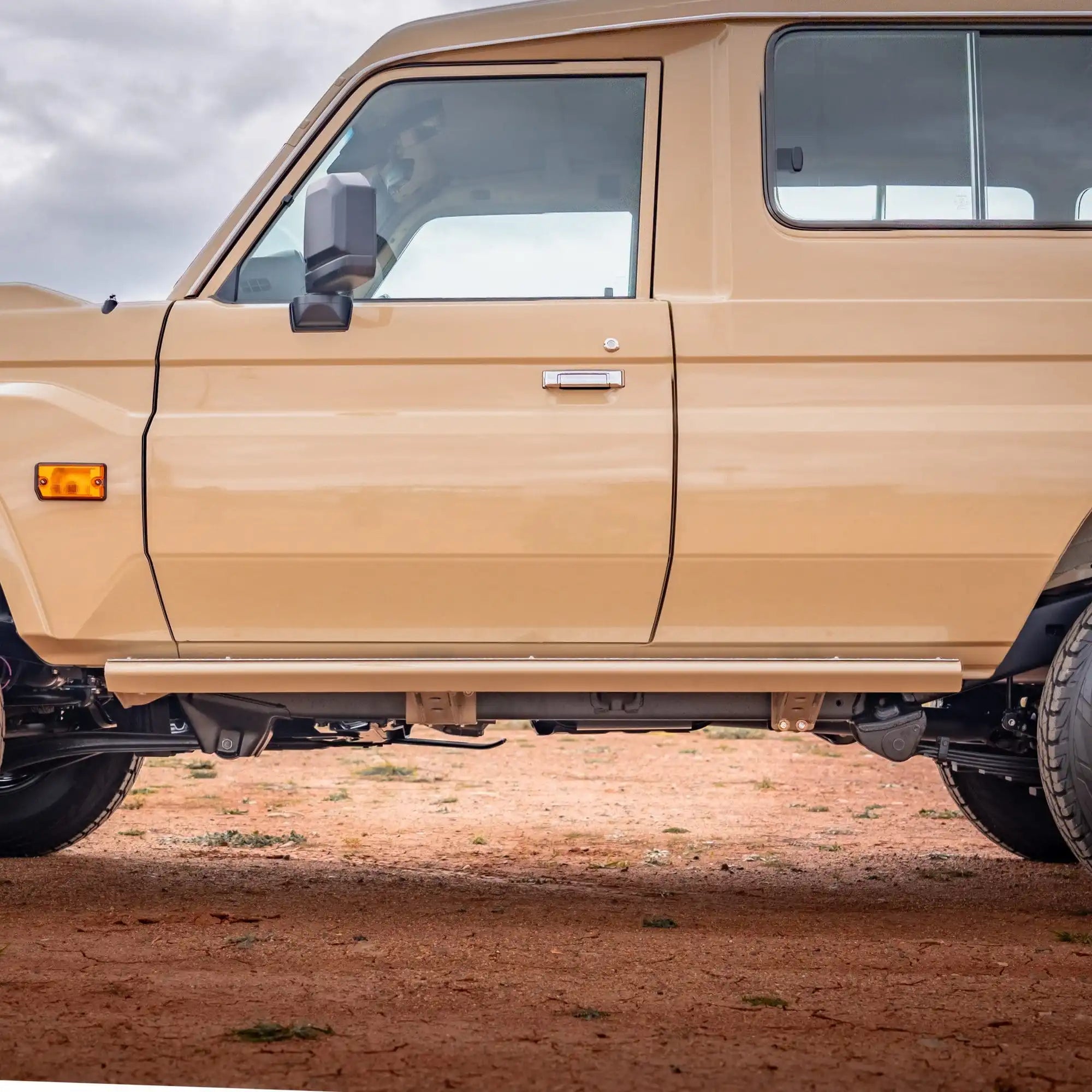 Beige truck parked on a dirt road with a cloudy sky.