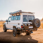 White off-road vehicle with roof rack and spare tire on a desert landscape