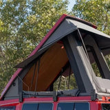Red vehicle with an open roof top tent against a tree-lined background