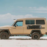 Beige off-road vehicle with a camper shell on a sandy beach with ocean and sky in the background