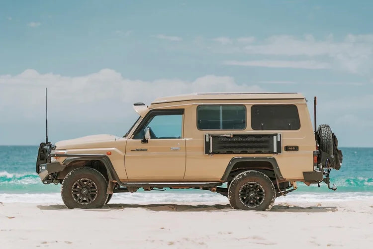 Beige off-road vehicle with a camper shell on a sandy beach with ocean and sky in the background