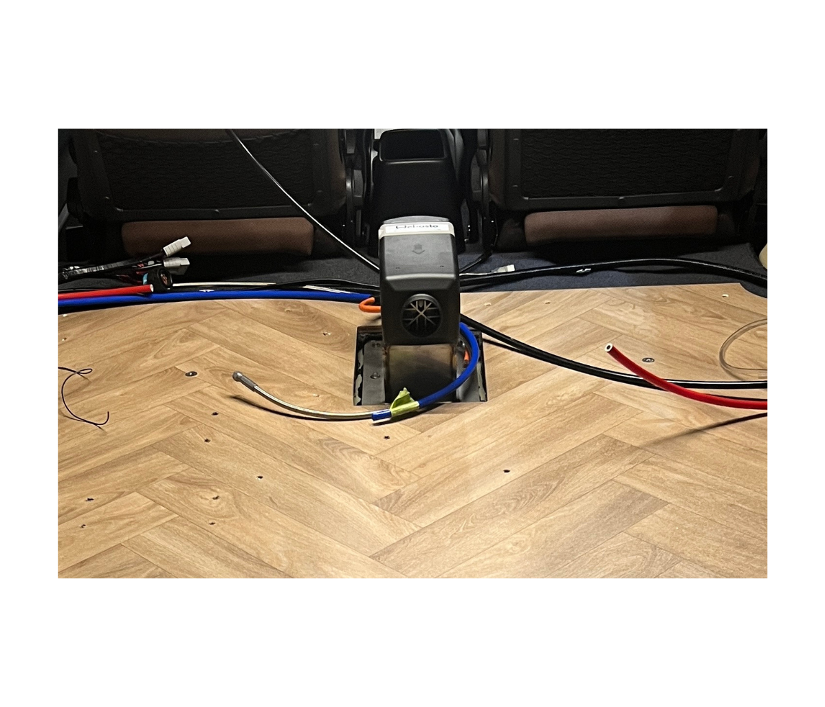 Car interior with wiring and a diesel heater on a wooden floor.