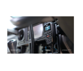 A Uniden XTRAK Pro UHF controller mounted in a vehicle cab, the backlit screen showing channel 25, with the coiled microphone lead running down beside the dash