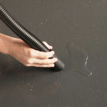 Person using a black vacuum cleaner on a dark surface with a visible water stain.