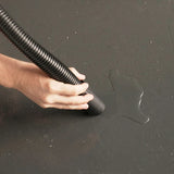 Person using a black vacuum cleaner on a dark surface with a visible water stain.