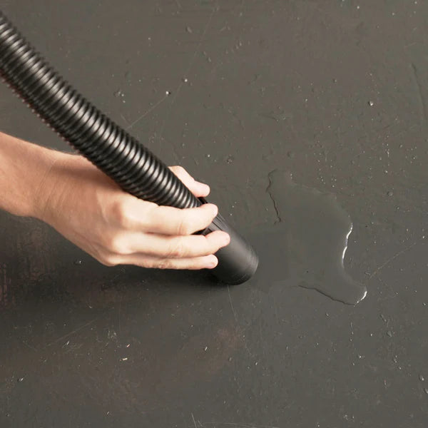 Person using a black vacuum cleaner on a dark surface with a visible water stain.