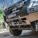 Close-up of a Nissan vehicle's front bumper with 'KIDDIN' license plate in an outdoor setting.