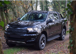 Black pickup truck parked in a forested area with Lazer Lamps Roof Mount Kit – Ford Ranger (2016–2022 with Roof Rails)