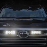 Close-up of a Toyota vehicle's front grille with illuminated headlights and Lazer Lamps Grille Kit – Toyota Land Cruiser 300 Series (2022+)