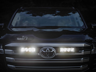 Close-up of a Toyota vehicle's front grille with illuminated headlights and Lazer Lamps Grille Kit – Toyota Land Cruiser 300 Series (2022+)