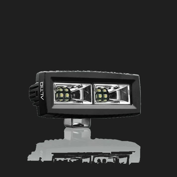ALTIQ CX4 scene work light at a three-quarter angle, the wide rectangular lens holding two reflector segments each with a cluster of LEDs, the ALTIQ name on the end cheek and the mounting bracket below