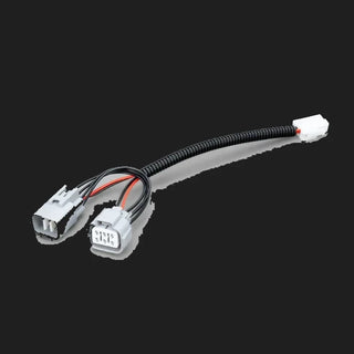 The Isuzu piggy-back adaptor laid out complete, two grey vehicle connectors at one end joined by a corrugated sleeve to a small white plug at the other