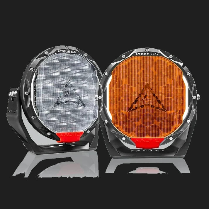 A pair of ALTIQ Rogue 8.5 lights side by side, one fitted with a clear ribbed panoramic cover and the other with an amber cover, both showing the ALTIQ arrow through the lens and a red trim tab at the base