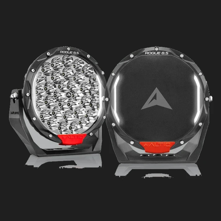 A pair of ALTIQ Rogue 8.5 driving lights side by side, one showing the reflector face with its dense cluster of LEDs and the ROGUE 8.5 marking on the bezel, the other fitted with a black cover carrying the ALTIQ arrow, both with red trim tabs at the base