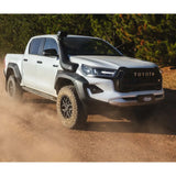 White Toyota truck driving on a dirt road with trees in the background