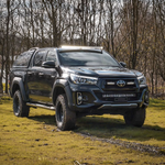Black Toyota pickup truck on a grassy field with trees in the background with Lazer Lamps Roof Mount Kit – Toyota Hilux (2015+ No Roof Rails)