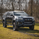 Black Toyota pickup truck on a grassy field with trees in the background with Lazer Lamps Roof Mount Kit – Toyota Hilux (2015+ No Roof Rails)