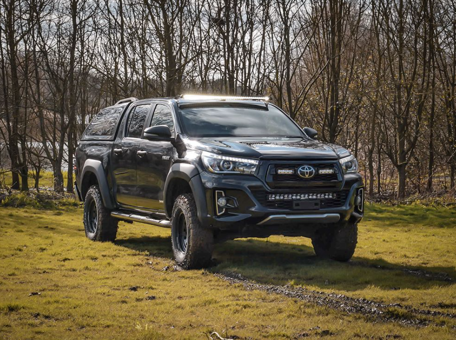 Black Toyota pickup truck on a grassy field with trees in the background with Lazer Lamps Roof Mount Kit – Toyota Hilux (2015+ No Roof Rails)