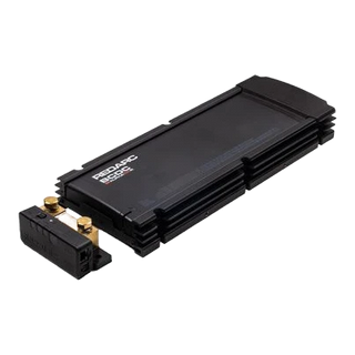 Redarc BCDC Alpha100 R battery manager seen from above at an angle, the long finned black case with the separate battery sense module and its two gold terminal studs sitting alongside