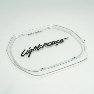 Clear Lightforce lens cover photographed at an angle, showing the depth of the moulded rim, the retaining clips around the edge and MADE IN AUSTRALIA embossed on the inner face