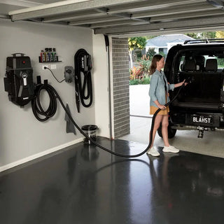 Woman using the Blahst K21 car vacuum in a garage with cleaning tools on the wall