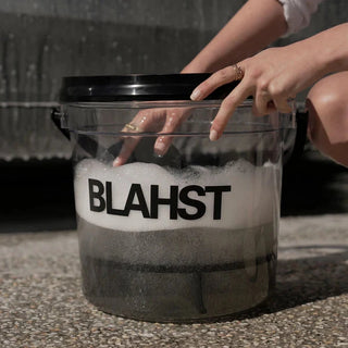 Person interacting with a transparent container labeled 'Blahst' filled with a foamy substance.