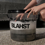 Person interacting with a transparent container labeled 'BLAHST' filled with a foamy substance.