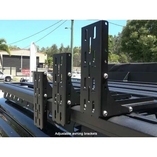 Adjustable awning brackets on a vehicle roof with a blurred background of trees and buildings.