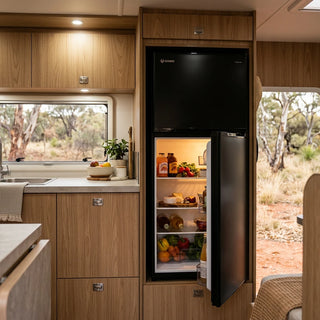 Bushman DC190L-X built into a caravan cabinet with the fridge door open, showing the stocked shelves and outback scrub through the window