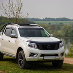 White Nissan pickup truck parked by a lake with trees in the background with Lazer Lamps Nissan Navara (2014-2019) Roof Mounting Kit