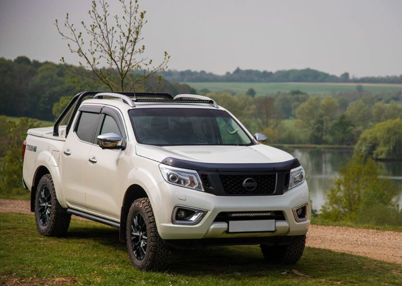White Nissan pickup truck parked by a lake with trees in the background with Lazer Lamps Nissan Navara (2014-2019) Roof Mounting Kit