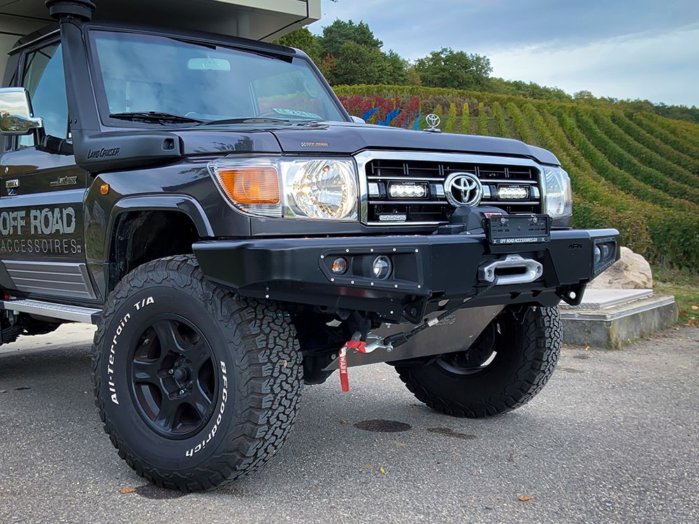 Black Toyota Land Cruiser off-road vehicle with large tires and Lazer Lamps Grille Mount Kit for Toyota LandCruiser 70 Series ST4 Evo on a paved surface.