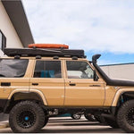 Beige LC76 with roof rack and additional equipment parked in front of a building.