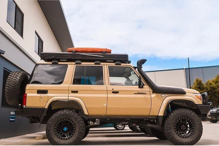 Beige LC76 with roof rack and additional equipment parked in front of a building.