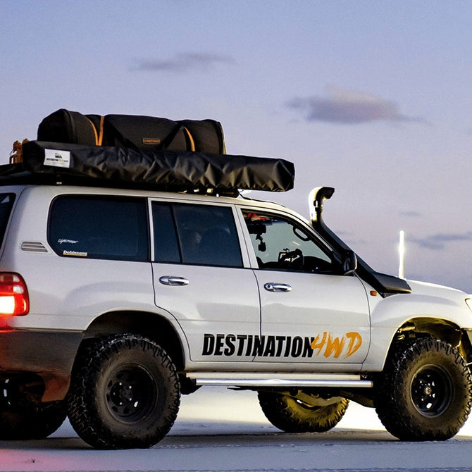 White SUV with 'Destination 4WD' branding and roof rack on a cloudy sky background