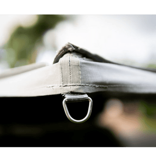 Close-up of a metal D-ring attached to a fabric surface with a blurred natural background