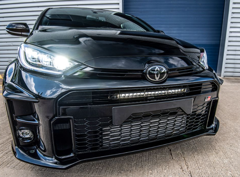 Black Toyota car with a prominent grille and headlights in front of a garage door.