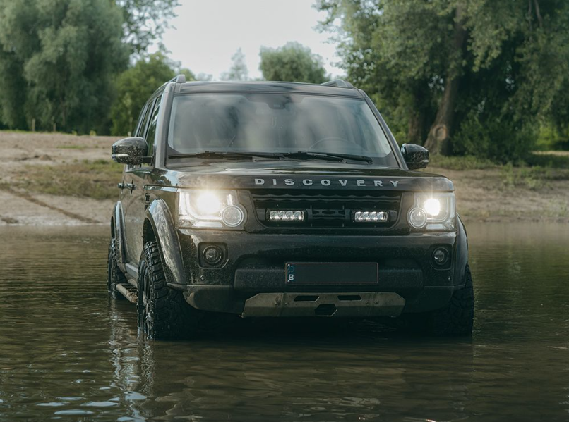 Land Rover Discovery driving through water with trees in the background