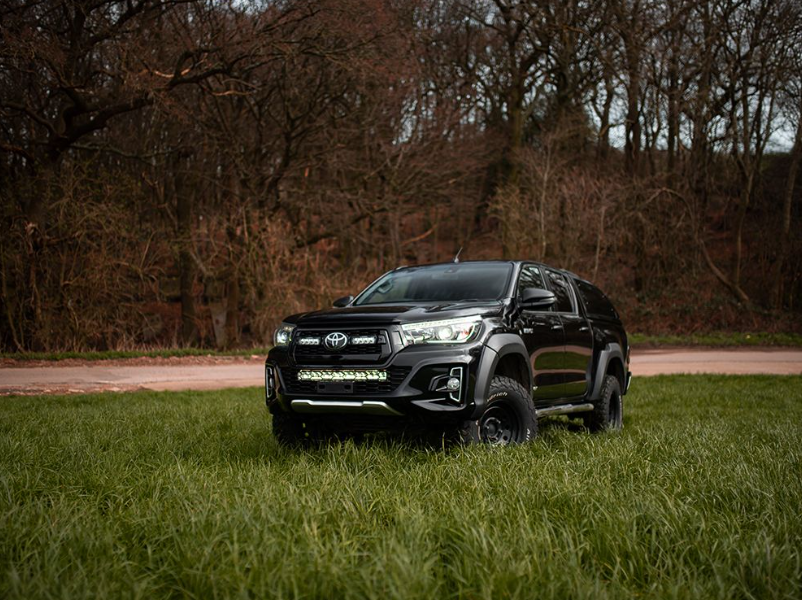 Black Toyota truck parked on a grassy area with trees in the background with Lazer Lamps Bumper Beam Mount Kit – Toyota Hilux (2017–2020)