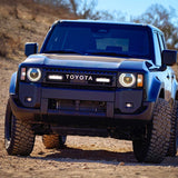 Blue Toyota Prado 250 on a dirt road with a clear sky and Lazer Lamps ST4 Evolution Grille Kit – Land Cruiser 250 (2024+)
